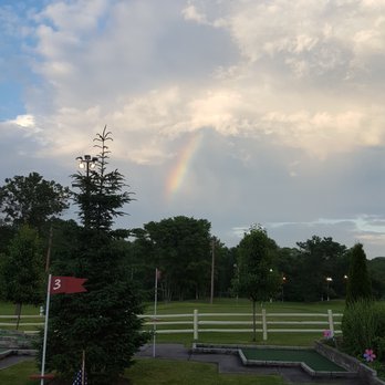 A miniature golf course beneath a partly cloudy sky and rainbow.